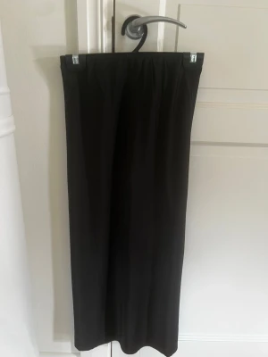 Svart Satinkjol från XOXO Friends - En stilren svart satinkjol från XOXO Friends med enkel och rak passform. Kjolen har resår i midjan för extra komfort och är tillverkad i ett mjukt, lätt material som passar perfekt till olika outfits.