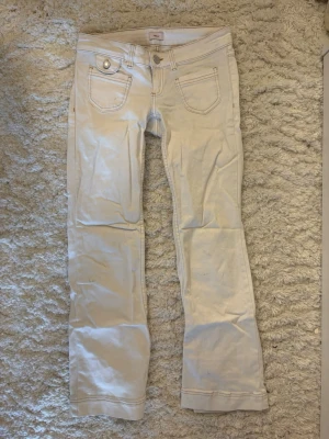 Vita bootcut jeans Nelly - Snygga vita jeans från Nelly med bootcut passform och dekorativ knappdetalj på ena framfickan. Klassisk femficksmodell med ljusa sömmar och normal midja. Tillverkade i ett mjukt bomullsmaterial med lite stretch för extra komfort.