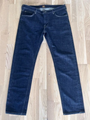 Mörkblå raka jeans från Lee - Snygga mörkblå jeans från Lee med klassisk rak passform och fem fickor. Jeansen har kontrastsömmar och är tillverkade i ett slitstarkt denimtyg. Perfekta för en clean och tidlös look. Knappt använda. Storlek W34 L32
