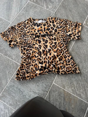 Leopardmönstrad t-shirt från Rabanne - Cool t-shirt från Rabanne med leopardmönster i bruna, svarta och beige toner. Storlek L men liten i storlek. T-shirten har korta ärmar och rund halsringning. Perfekt för dig som vill sticka ut med en trendig och djärv look.