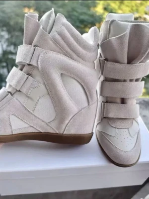 Beige höga sneakers Isabel Marant - Snygga höga sneakers från Isabel Marant i beige mocka och textil. Skorna har flera kardborreband och en chunky sula i gummi. Designen är futuristisk och trendig, perfekt för dig som vill sticka ut med din stil. För fler bilder skriv.