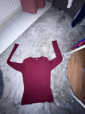 Vinröd ribbstickad tröja XS - Säljer en vinröd ribbstickad tröja med lång ärm och rund hals. Tröjan är figurnära och har en enkel, stilren design som passar perfekt till jeans eller kjol. Materialet är mjukt och stretchigt för extra komfort.