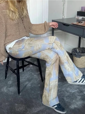 Svincoola byxor från Acne Studios - Unika byxor från Acne Studios med abstrakt mönster i beige, blått och brunt. Modellen har utsvängda ben. 
