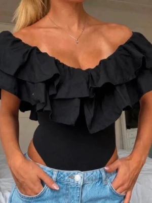Svart body med volangdetaljer - Trendig svart body med stora volangdetaljer runt axlar och urringning. Off shoulder-modell som ger en snygg och unik look. Tillverkad i stretchigt material som sitter tight mot kroppen. Perfekt att styla med jeans eller kjol för en cool outfit.