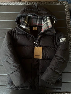 Burberry dunjacka - Säljer en snygg svart dunjacka från Burberry! Jackan är i mycket bra skick och har inga defekter. Man kan även ta av armarna så de blir en väst (bild 2)  varm så perfekt till vinter/höst! Om ni har några frågor så hör av er😊