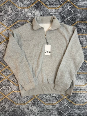 Grå halvzip tröja - En stilren grå tröja med halvzip och hög krage. Tillverkad i mjukt sweatshirtmaterial som känns skönt mot huden. Perfekt för dig som gillar en enkel men snygg look. Ribbstickade muddar vid ärmslut och nederkant för extra komfort.