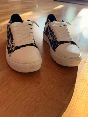 Numeris  - Snygga sneakers i svartvitt med coolt mönster på sidorna och vit tå samt vit sula. Skorna har grova vita snören och låg profil. Ovandelen verkar vara i textil och syntet, perfekt för en trendig streetstyle-look.