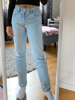 Ljusblå Levi's 501 jeans  - Snygga ljusblå jeans från Levi's med klassisk femficksdesign och medelhög midja. De har en rak passform och är tillverkade i slitstarkt denim. Är lite för korta på mig men passar säkert någon som är kortare än 170 cm. Stängs med knappar. 