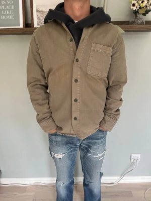Mango Man Overshirt Jacka Brun/Beige Regular Fit M - Snygg MNG Man overshirt/jacka i brun/beige ton. Enkel och stilren design med klassisk krage, knappstängning och bröstficka. Regular fit som gör den lätt att bära över exempelvis hoodie eller t-shirt.  Ett mångsidigt plagg som passar bra till jeans, chinos och sneakers.  Storlek: M Passform: Regular fit Färg: Brun/beige Skick: Mycket fint skick  📦 Skickas snabbt och välpackat.