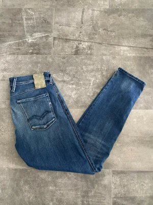 Replay Jeans - Säljer ett par klassiska blå jeans från Replay i modellen anbass. Säljer de pågrund av de inte kommer till användning. Där finns något litet hål på höger ben, se sista bild men är inget som påverkar helhetsintrycket. Annars bra skick, storlek 32/32. Kanske en aning större i passformen.