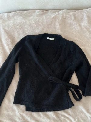 Svart omlottkofta - Gina Tricot - Säljer en mysig svart stickad omlottkofta från Gina tricot 💕Koftan har långa ärmar och ribbade kanter. Perfekt att slänga över en topp för en enkel men snygg look, Storlek: M men har krympts i tvätten så passar bra som en S🪷 Priset kan diskuterar och meddela mig vid frågor, fler bilder eller bud :)
