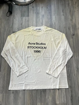 Acne studios tröja  - Vit långärmad topp från Acne Studios med tryck 'STOCKHOLM 1996' i svart framtill. Klassisk rund halsringning och relaxed fit. Perfekt för dig som gillar minimalistisk och stilren design.