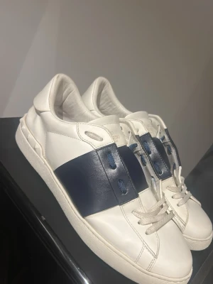 Valentino Open skor - Snygga vita sneakers med bred mörkblå läderdetalj över mitten och matchande blå snörhål. 
