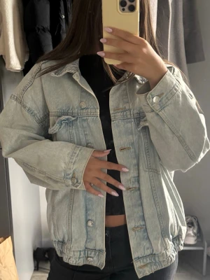 Oversized ljusblå jeansjacka - Säljer en oversized ljusblå jeansjacka med klassisk krage, knappstängning och två bröstfickor med lock. Jackan har en avslappnad passform och elastisk nederkant för en cool och trendig look. Perfekt att slänga över en hoodie eller crop top.