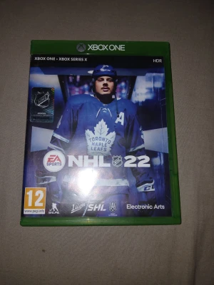 NHL 22 till Xbox One/Xbox Series X - NHL 22 till Xbox One och Xbox Series X är ett ishockeyspel där du kan spela som ditt favoritlag i NHL. Omslaget pryds av en spelare från Toronto Maple Leafs. Spelet har en grön plastbox och skivan har samma motiv som omslaget.