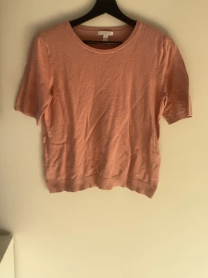 Ljusrosa stickad topp från H&M - Söt ljusrosa stickad topp från H&M Basics med rund halsringning och korta ärmar. Perfekt till jeans eller kjol för en enkel och fräsch look. Mjuk och bekväm, passar till många olika stilar.
