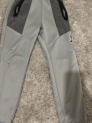 Grå Nike Air Max mjukisbyxor - Snygga grå mjukisbyxor från Nike Air Max med mörkgrå detaljer och svarta dragkedjor på fickorna. Tillverkade i ett mjukt och stretchigt material som passar perfekt för chill eller träning. Luftig passform och modern look.