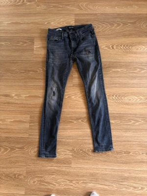 Mörkblå Jack and Jones slim fit jeans - Snygga mörkblå slim fit jeans med slitningar på låren och knäna. Klassisk femficksmodell med dragkedja och knapp i midjan. Jeansen har en tvättad look och smal passform som ger en modern stil.