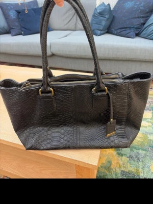 Svart handväska i ormmönstrat läder - Snygg svart handväska i ormmönstrat läder med guldfärgade detaljer från Åhléns 💕