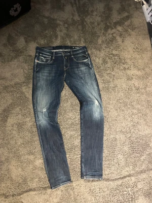 Blå slitna replayjeans - Säljer ett par blå skinny jeans med slitningar och snygg tvätt. Jeansen har fem fickor, dragkedjegylf och kontrastsömmar. Perfekta för en avslappnad och trendig look.