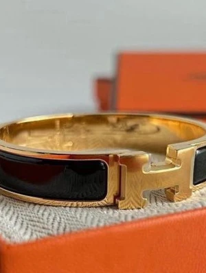 Svart och guld armband med H-detalj - Snyggt armband i svart emalj och guldfärgad metall med en stor H-detalj framtill. Armbandet har en stilren och elegant design som verkligen sticker ut. Perfekt accessoar för dig som gillar exklusiva detaljer och klassisk stil.