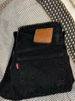 Svarta Levi's 501 jeans - Säljer ett par klassiska svarta Levi's 501 jeans med raka ben och hög midja. Jeansen har fem fickor, knappgylf och den ikoniska röda Levi's-lappen på bakfickan. Tillverkade i slitstark denim som ger en tidlös look.