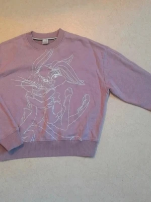Looney Tunes x BOSS y2k vintage sweatshirt - Säljer en lila hoodie från Looney Tunes x BOSS med tryck av Bugs Bunny och Lola Bunny på framsidan. Tröjan har rund halsringning, ribbade muddar och är gjord i mjukt bomullsmaterial. Perfekt för dig som gillar streetwear och tecknade motiv.