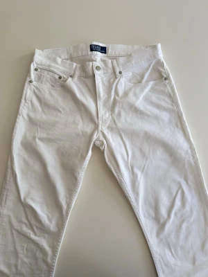 Vita raka jeans från Polo Ralph Lauren - Säljer ett par vita jeans från Polo Ralph Lauren med klassisk femficksmodell och raka ben. Jeansen har silverfärgade nitar och knapp, samt diskret logga på myntfickan. Perfekta för en clean och stilren look. STORLEK 32/32