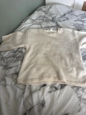 Krämvit stickad tröja från H&M - Mysig krämvit stickad tröja från H&M med rund halsringning och ribbade muddar vid ärmslut och nederkant. Perfekt för lager på lager och enkel att matcha med olika outfits. Klassisk och stilren design som passar till det mesta.