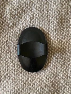 Svart oval gummiskrapa för häst - En svart oval gummiskrapa med handtag, perfekt för att borsta och ta bort smuts från häst borstar. Skrapan har räfflad yta på ena sidan och ett greppvänligt handtag på andra sidan. Tillverkad i slitstarkt gummi och enkel att använda.