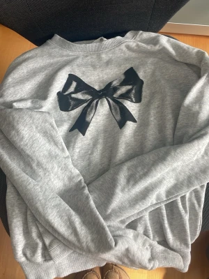 Grå roset tröja - Grå tröja med en fin roset i mitten, tyvärr har den en liten fläck på ärmen💓