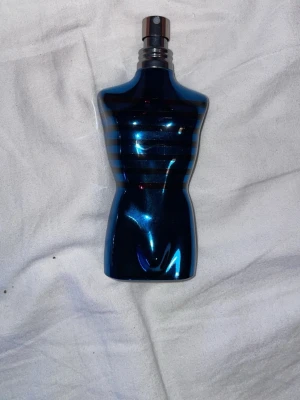 Jean Paul Gaultier Le Male parfym - En ikonisk parfym från Jean Paul Gaultier i en blå, kroppformad flaska med silverfärgade ränder. Flaskan har en metallisk finish och kommer med en silvrig cylinderformad förpackning. Perfekt för dig som gillar unika och snygga flaskor.