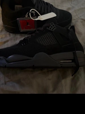 Svarta Air Jordan 4 sneakers - Snygga helsvarta Air Jordan 4 sneakers med meshpaneler och detaljer i mocka och läder. Skorna har en robust sula och klassisk siluett med högt skaft och ikonisk Jumpman-logga på plösen. Perfekta för dig som gillar streetwear och sportig stil.