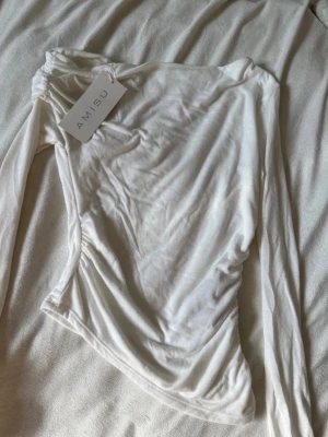 Amisu vit asymmetrisk topp strl M – ny med prislapp - Vit asymmetrisk topp från Amisu i storlek M.  Figurnära modell i tunt, stretchigt material med asymmetrisk design och en lång ärm. Snygg både till vardags och mer uppklätt med jeans, kostymbyxor eller kjol.  Helt ny och oanvänd med prislappen kvar.