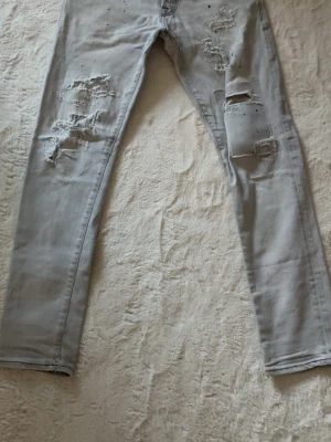 Ljusa slitna jeans från Jack & Jones Glenn - Säljer ett par ljusgrå jeans från Jack & Jones med skinny fit och slitna detaljer på både lår och knän. Jeansen har klassisk femficksmodell, dragkedja och knappgylf. Perfekta för en trendig och avslappnad stil.