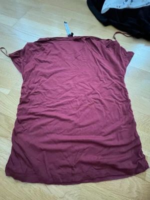 Vinröd kortklänning från 152 - En enkel vinröd tröja från lager 152 i mjukt material. Tröjan har korta ärmar och rak passform, perfekt för en avslappnad look. Passar dig som gillar minimalistisk stil och vill ha något bekvämt och snyggt.