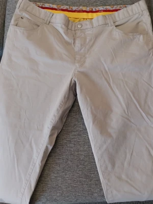 Meyer chinos beige storlek 29 - Snygga beige chinos från Meyer med klassisk rak passform och detaljerad insida i midjan med färgglada mönster. Byxorna har fickor fram och bak samt bälteshällor. Perfekta för en clean och stilren look. Storlek 29 se bilder 