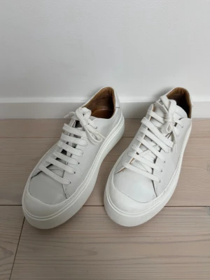 Vita sneakers från Tiger of Sweden - Stilrena vita sneakers från Tiger of Sweden i slätt läder med tjock vit sula och klassisk snörning. Insidan är fodrad i beige/brunt läder för extra komfort. Perfekta för en clean och modern look. Innermått 25,7. Nypris 2800 kr.