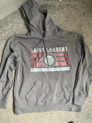 Saint Laurent hoodie - Säljer min ysl hoodie som är i storlek M dock är den lite liten i storleken. Extremt bra skick bortsett från metall delarna på snörena då de är lite tillplattade men de går säker att fixa eller om man inte orkar så kan man köpa nya extremt billigt, tröjan är i 100% bomull. Skriv vid funderingar!