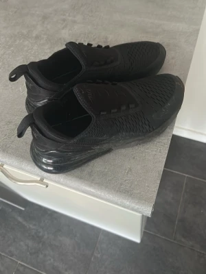 Helvita svarta sneakers med mesh - Säljer ett par helsvarta sneakers med sportig design och meshmaterial för bra ventilation. Skorna har en tjock sula och elastisk ovandel utan klassiska skosnören, vilket ger en clean look. Perfekta för dig som gillar streetwear och bekväma skor.