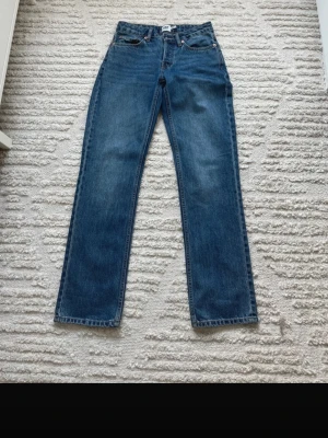 Blå raka jeans i klassisk modell - Säljer ett par blå jeans med rak passform och fem fickor. Jeansen har en klassisk midja och är tillverkade i slitstarkt denimtyg. Perfekta för dig som gillar en tidlös och enkel stil. Passar till det mesta och är riktigt bekväma.