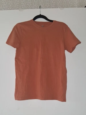 Orange basic t-shirt - En enkel och stilren orange t-shirt med rund hals och korta ärmar. T-shirten har en normal passform och är tillverkad i mjuk bomull, perfekt för en avslappnad look.