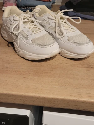 Vita sneakers med meshdetaljer - Fräscha vita sneakers med snygga meshdetaljer på ovandelen. Skorna har klassisk snörning och en sportig vibe, perfekta för en trendig streetstyle-look. Materialmix av syntet och mesh ger både stil och komfort.