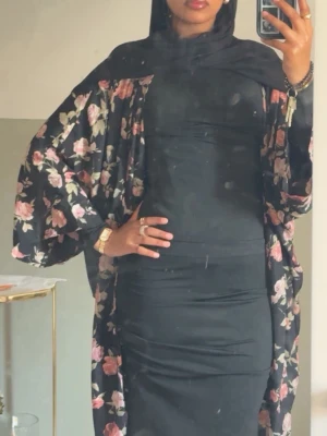 Svart långklänning med blommigt mönster - Snygg svart långklänning med blommigt mönster i rosa och beige toner. Klänningen har lång ärm och en åtsittande passform med en elegant, modest look. Perfekt för dig som gillar stilrena och feminina detaljer.