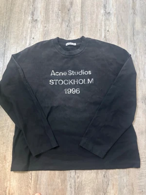 Svart sweatshirt Acne Studios - Cool svart sweatshirt från Acne Studios med trycket 'Acne Studios STOCKHOLM 1996' på bröstet. Tröjan har rund halsringning och långa ärmar. Perfekt för dig som gillar minimalistisk och stilren design. Materialet känns mjukt och bekvämt.