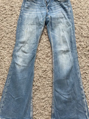 Ljusblå bootcut jeans - Säljer ett par ljusblå bootcut jeans med klassisk femficksmodell och snygga slitningar. Jeansen har en broderad detalj på bakfickan och är tillverkade i denim med skön stretch. 