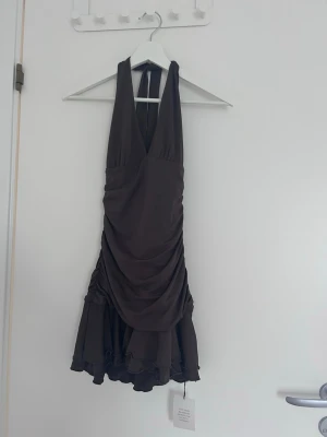 Svart kort omlottklänning - Snygg svart kort klänning med omlottdesign och djup v-ringning. Klänningen har halterneck och draperade detaljer som ger en elegant look. Perfekt för dig som vill sticka ut med en stilren och trendig outfit.