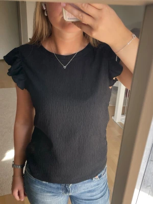Svart blus  - Säljer en fin svart blus med volanger från Pieces i storlek S. Fint skick och inga defekter!