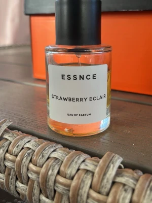 ESSNCE Strawberry Eclair parfym - En söt parfym från ESSNCE med doften Strawberry Eclair. Flaskan är cylindrisk i genomskinligt glas med svart lock och vit etikett. Innehållet är ljusgult och ger en fräsch och ungdomlig känsla. Perfekt för dig som gillar fruktiga och gourmanddofter.