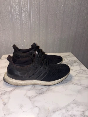 Adidas ultra boost - Snygga svarta sneakers med stickad ovandel och vit, dämpad sula. Skorna har klassisk snörning och diskreta detaljer på sidan. Perfekta för dig som gillar sportig och stilren look. Materialet är mesh och syntet.